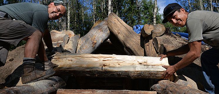 Course instructor Vince Prince, left, and Curtis Seymour place logs onto the pit house entrance.