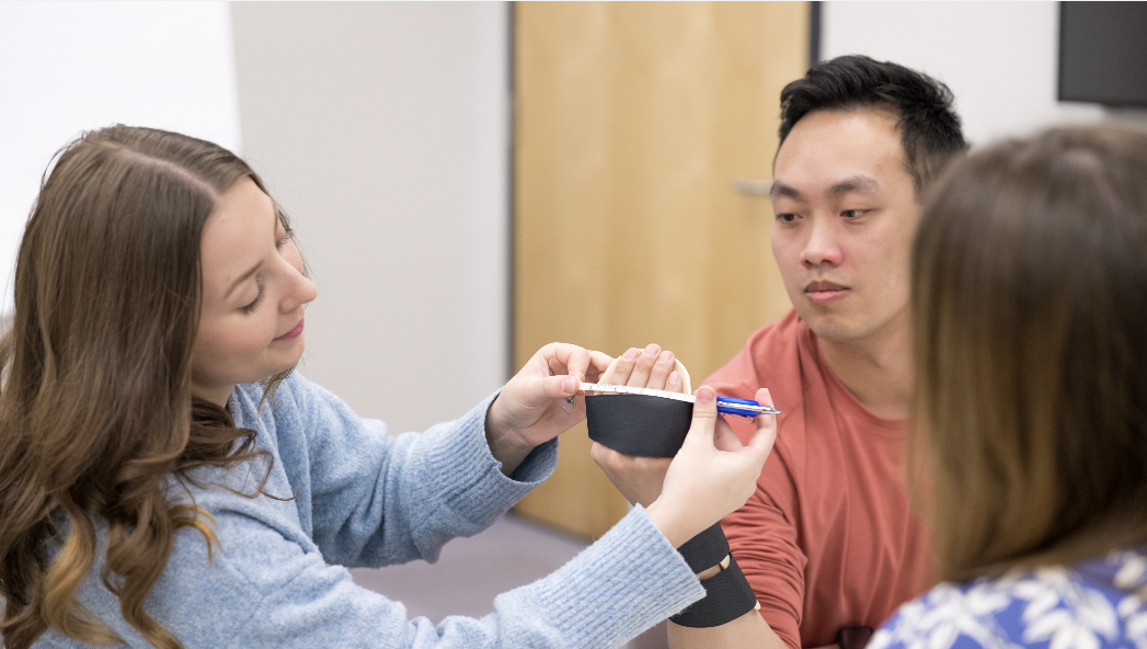 OT student practices clinical skills with fellow student, with a preceptor observing.