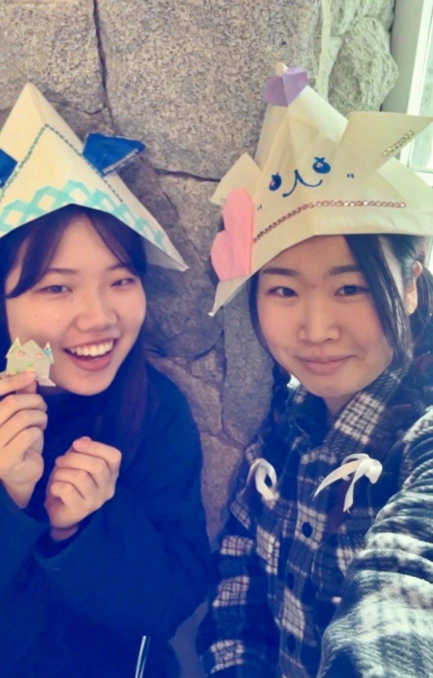 Two students in origami hats holding an origami frog