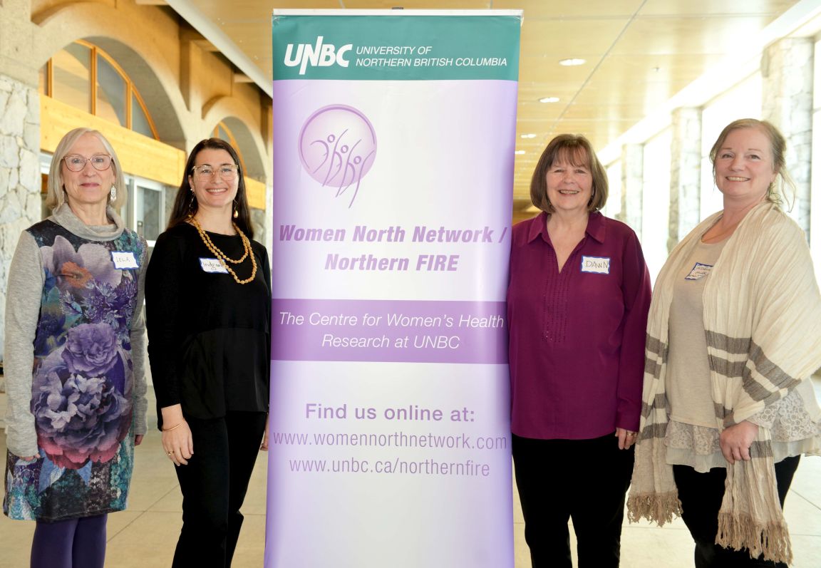 Four women stand next to a purple banner that reads Northern FIRE feminist institute for research and evaluation