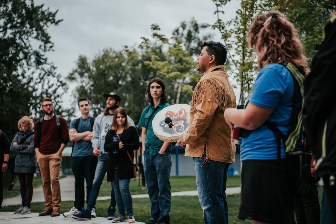 UNBC students standing in a circle with an Indigenous person playing the drum