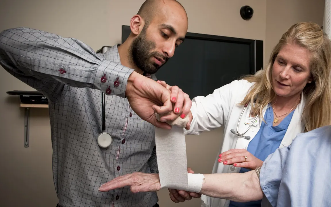 A medical student tapes an arm while a preceptor observes.