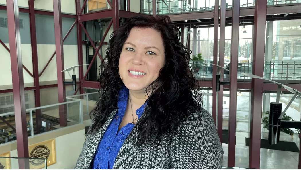 Abby Lodge wears a blue shirt and grey jacket, standing inside a building atrium.