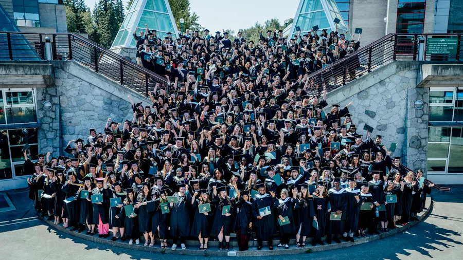 Large group of University students wearing black robes and caps stand on an exterior staircase