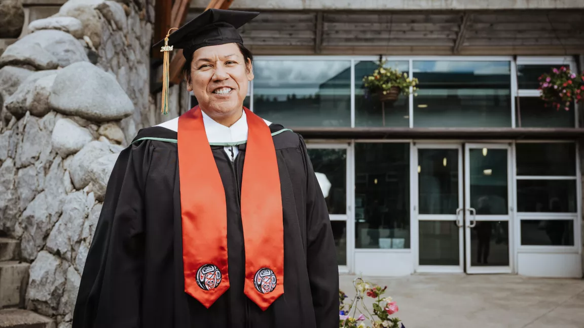 A person in academic cap and gown, wearing a red stole outside at the Prince George campus. 