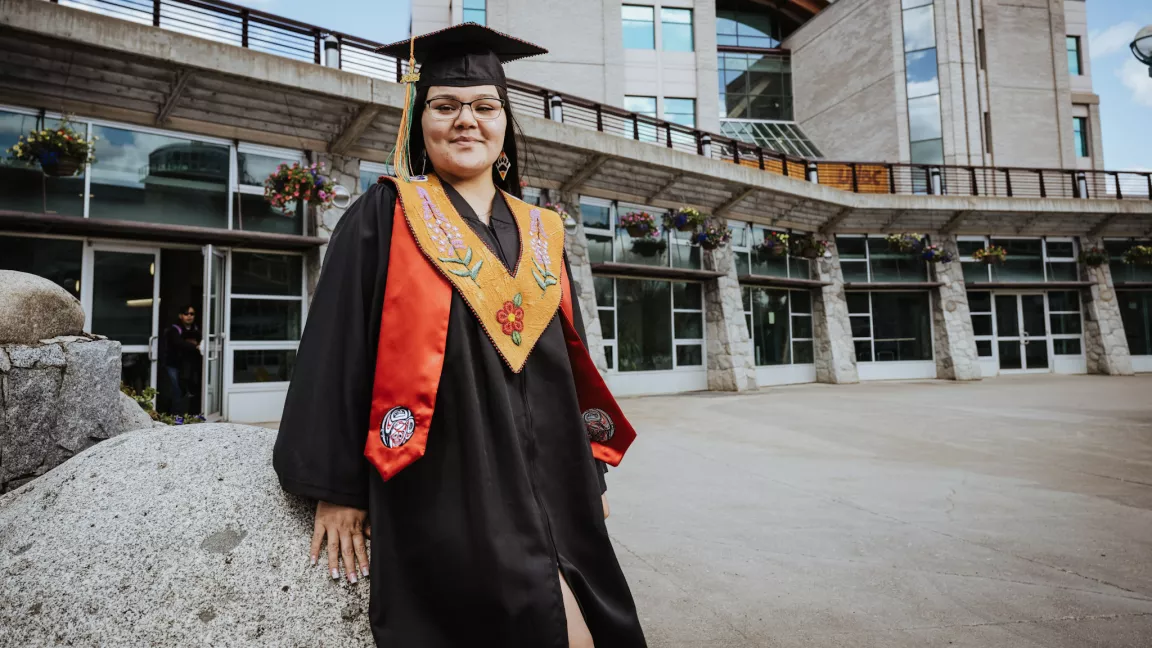 Person in academic cap and gown, wearing a leather beaded xxx and a red stole.  