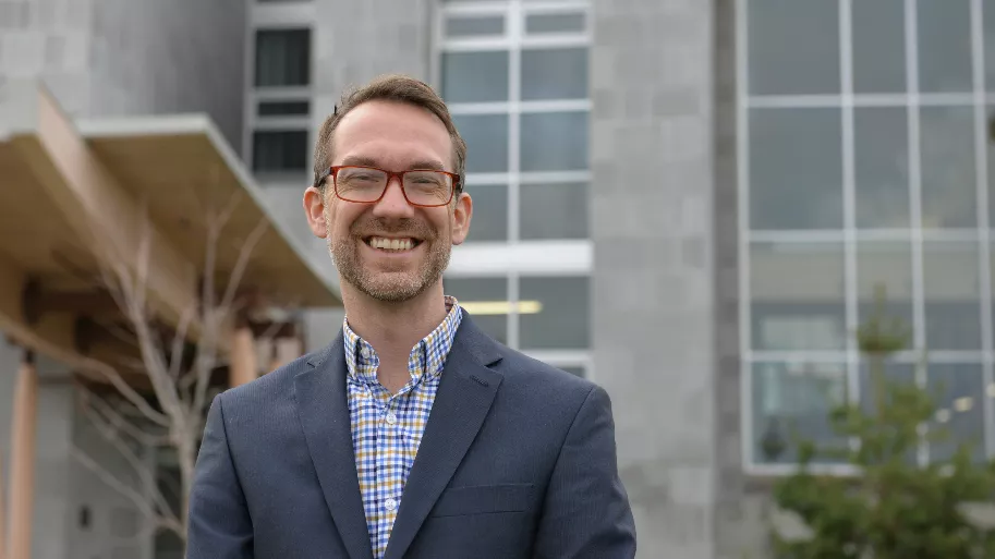 Dr. Rob Olson stands in front of grey brick building with large windows.