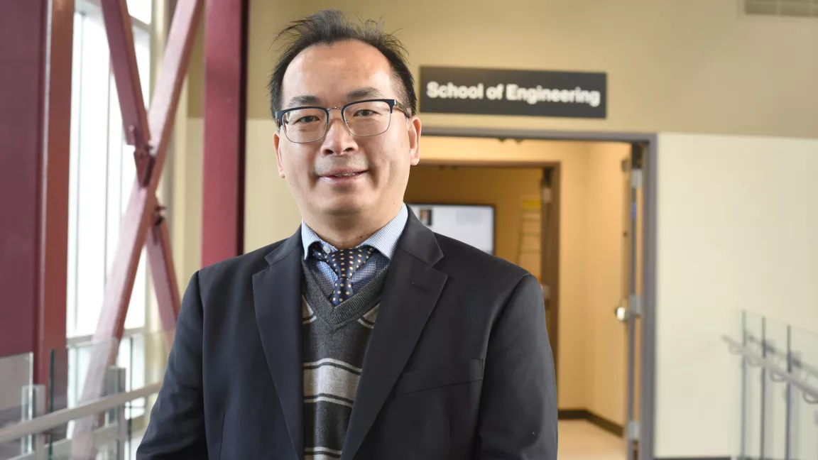 Dr. Jianbing Li in a suit and tie in front of the School of Engineering sign.