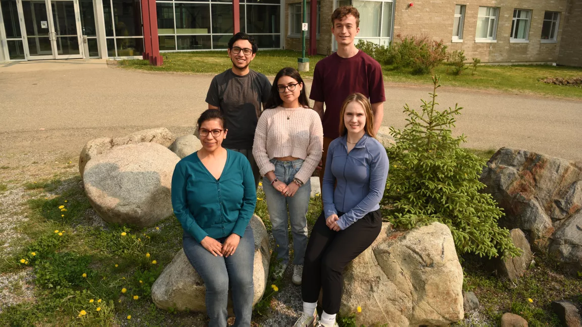 Five people pose, two sitting on rocks, three standing. 