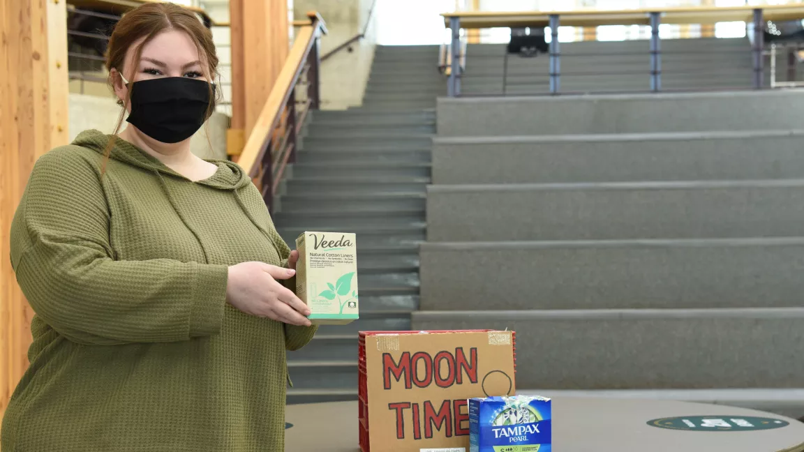 Social Work student Emily Erickson holds up menstrual products in the Canfor Winter Garden