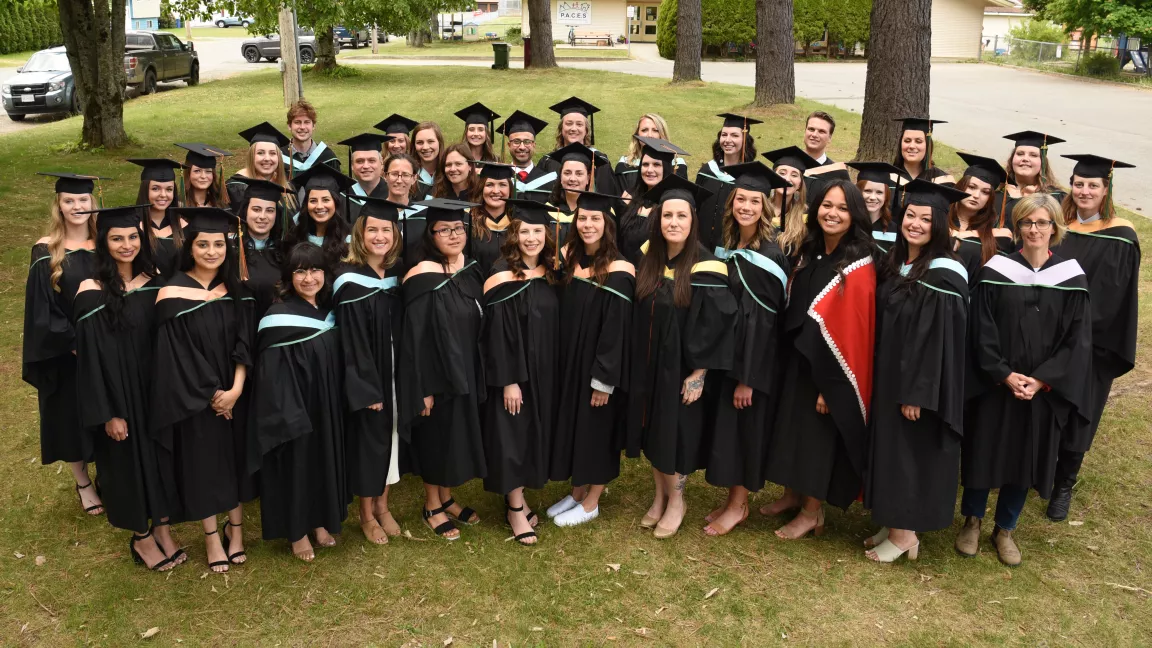 Group photo, outside, of graduates wearing academic caps and gowns.