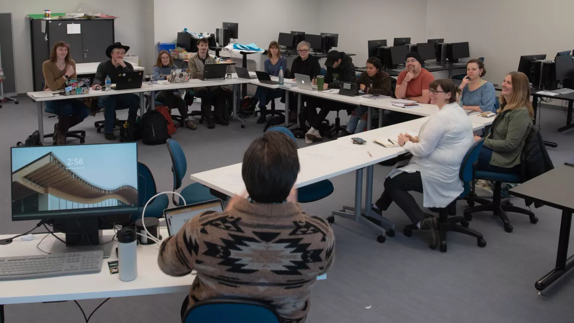 Students sit around a U-shaped table in a classroom with an instructor at the front. 