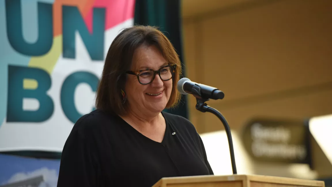 Dr. Margo Greenwood at a podium with UNBC banner in the background 