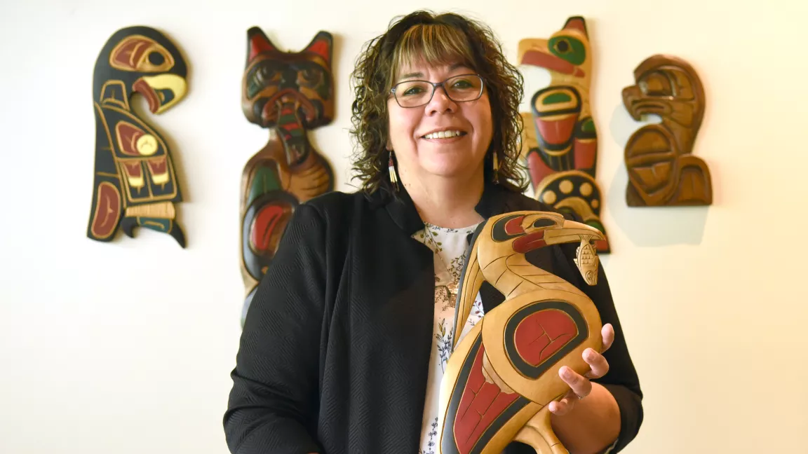 Bev Best holds a carved heron with four pieces of artwork behind her