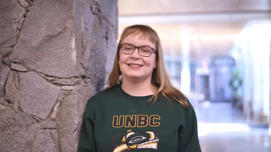 A student standing next to a stone pillar with a hallway behind 