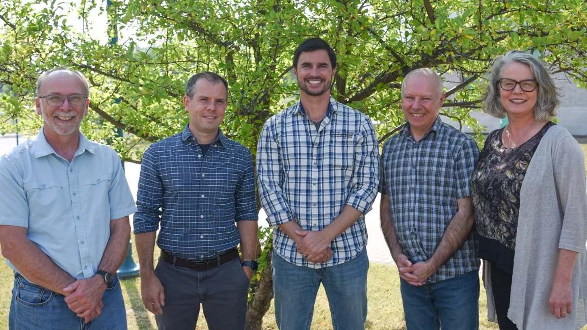 Five people stand outside with a tree in the background