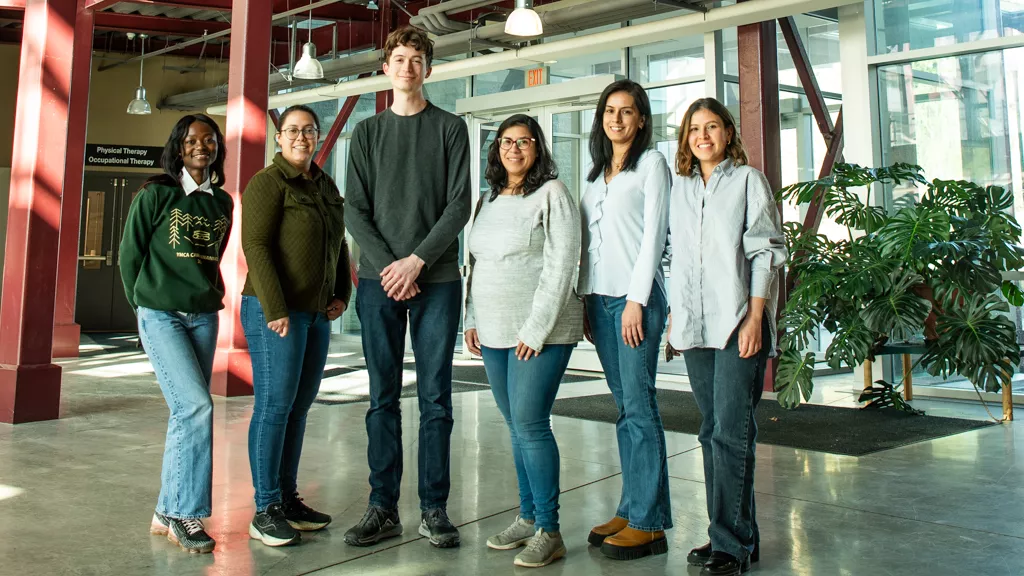 Group of six individuals stand in the glass atrium of UNBC's Teaching and Learning Building