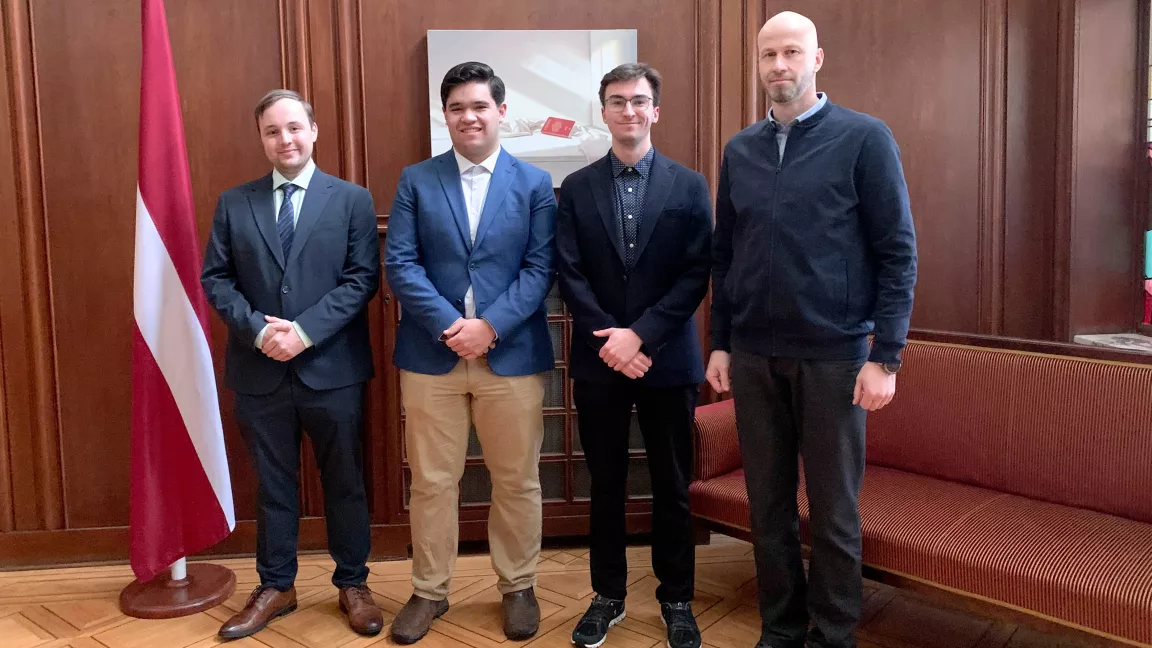 Four people standing in an office next to a Latvian flag.