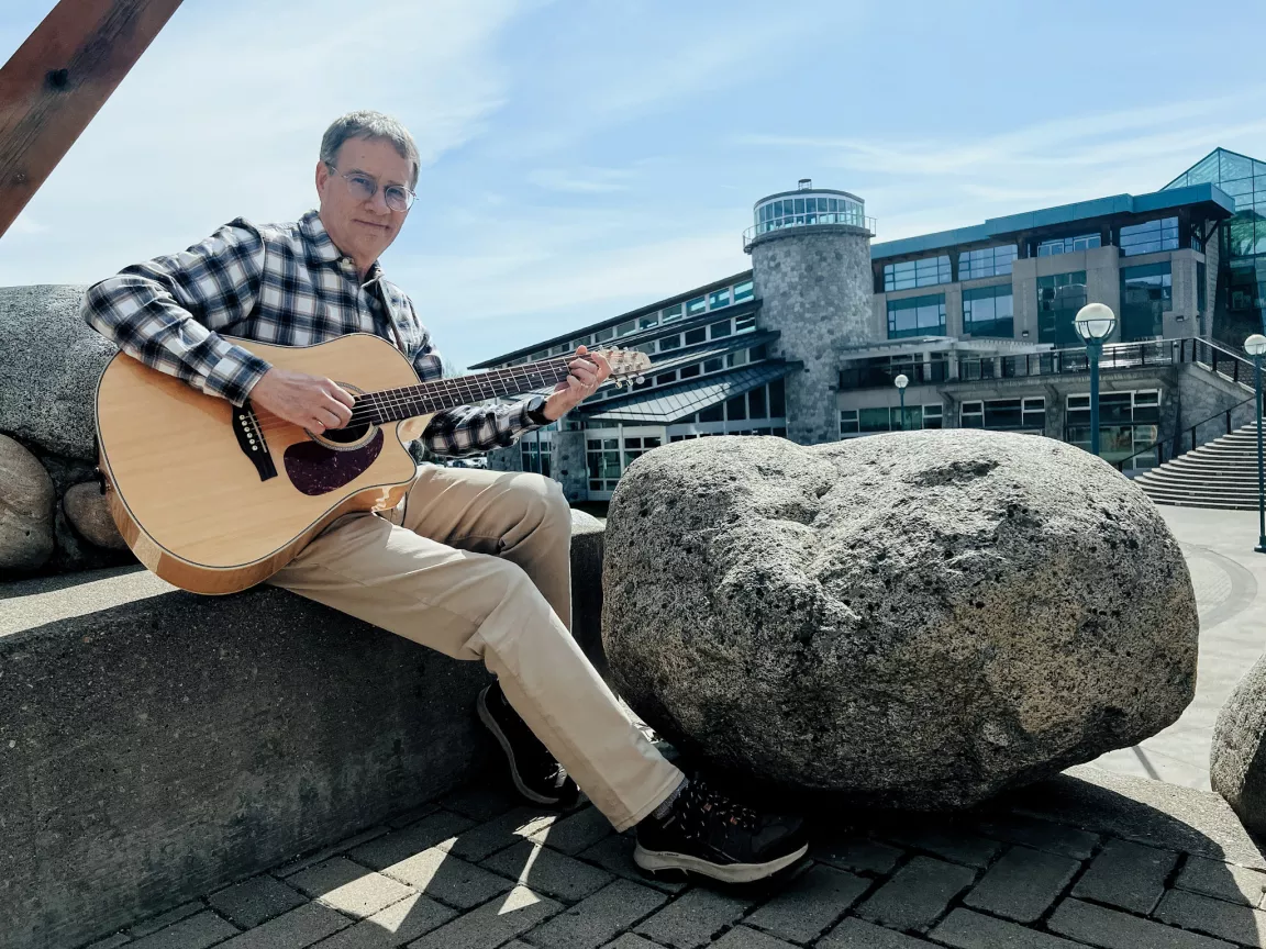 Dr. Kevin Hutchings with a guitar outside at UNBC's Prince George campus. 