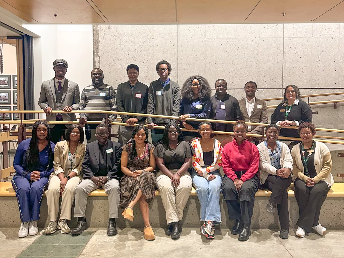 Photo shows large group of people in two rows. Front row is seated, back row is standing.