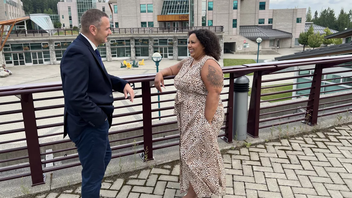 Two people standing, chatting with a university campus in the background