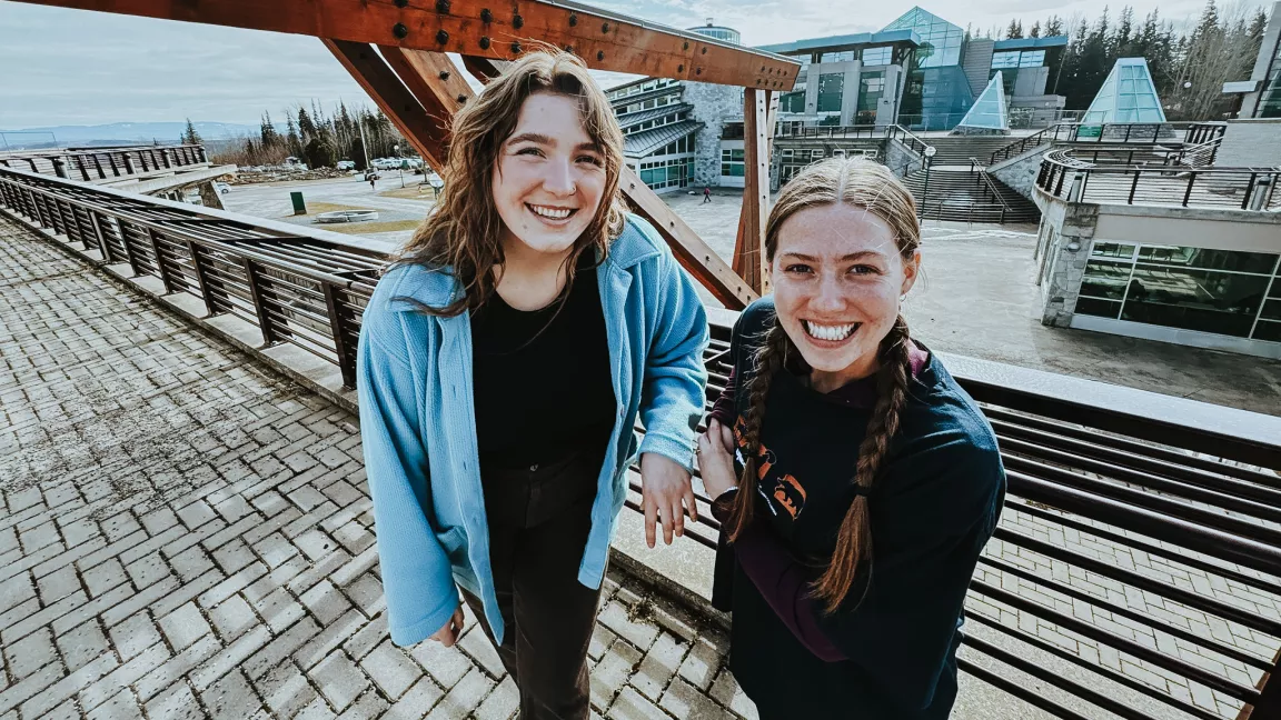 Two people outside at UNBC's Prince George campus with the Agora courtyard in the background. 