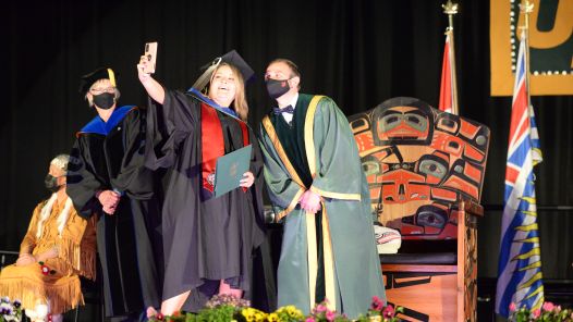A graduate takes a selfie with the president at Convocation 