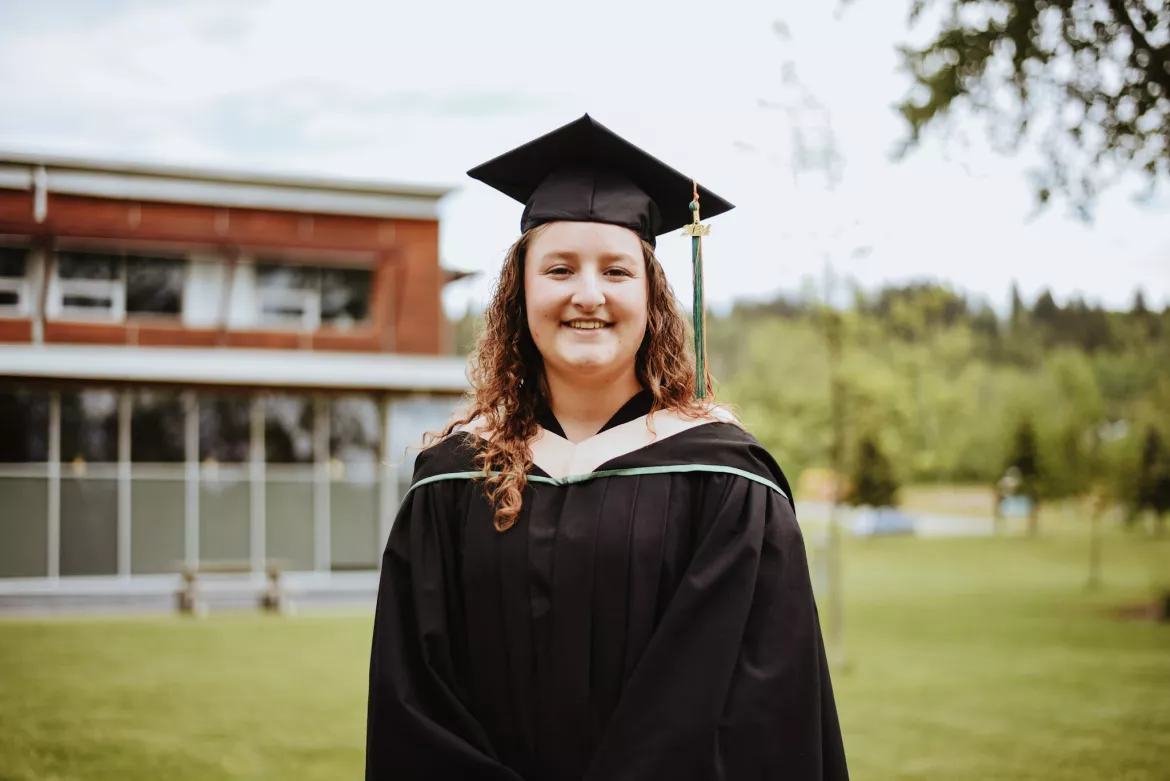 Person in academic cap and gown in front of Quesnel Campus 