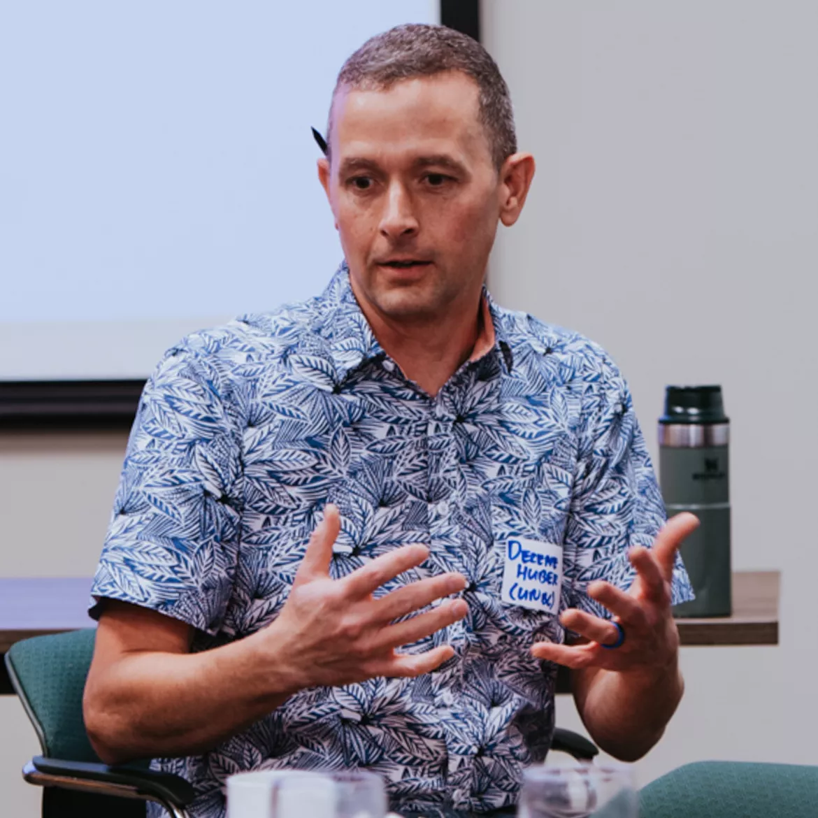 Person wearing blue and white patterned shirt gestures with hands.