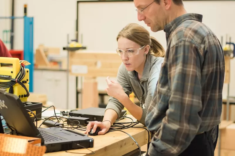 Student and instructor work on a problem at a laptop in a classroom lab.