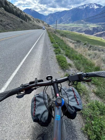 The front of a bike is shown in front of a long highway with mountains in the background.