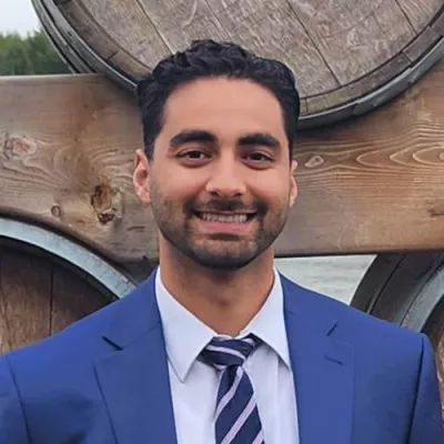 Indiividual wearing a blue suit and tie standing against wood backdrop.