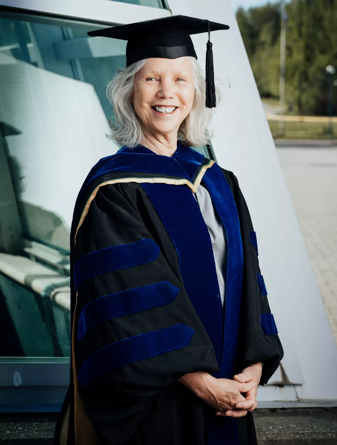 Person wearing black academic regalia and cap poses outside.