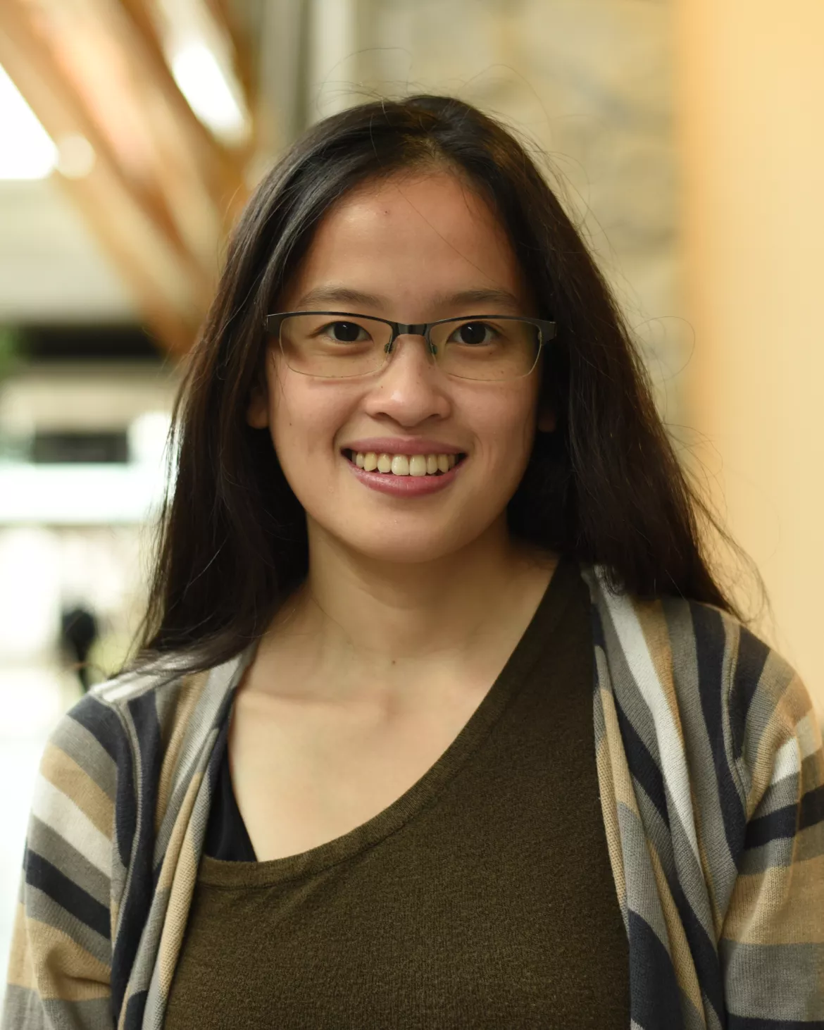 Person wearing brown top and striped sweater stands in hallway.