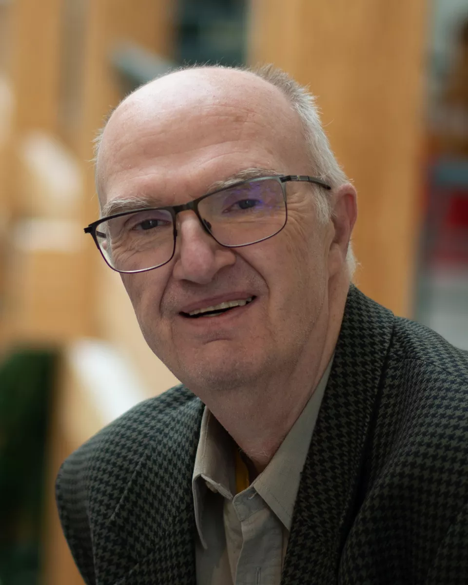 Close up photo of person wearing glasses, tan dress shirt and brown blazer.