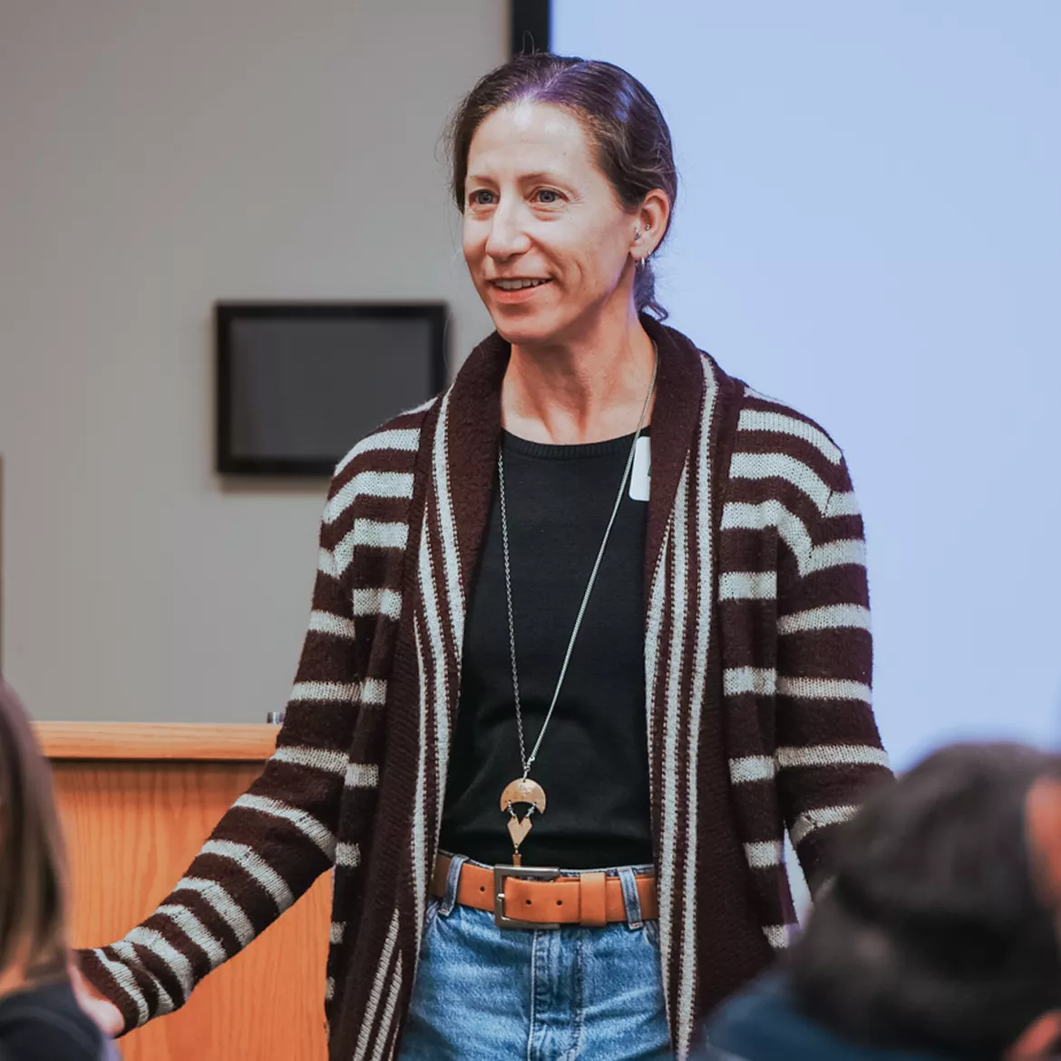 Person wearing black top, pendant, striped sweater and denim skirt.