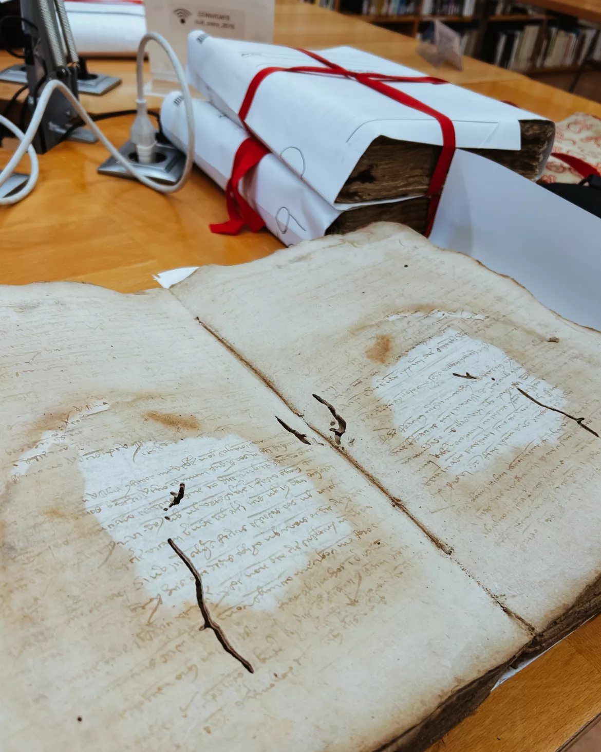 photo shows very old book on a table with other books bound in white paper with red ties in top right-hand corner.